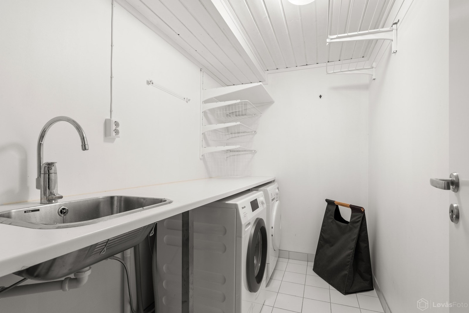 Praktisk vaskerom fra 2019 med flislagt gulv med gulvvarme, utslagsvask og opplegg for vaskemaskin. Galleribilde