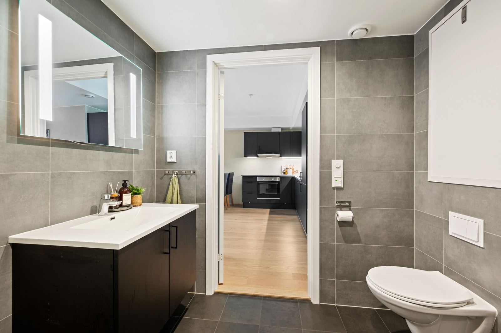 Badet er innredet med servantinnredning, speil med integrert belysning, veggmontert toalett og dusjhjørne. Galleribilde