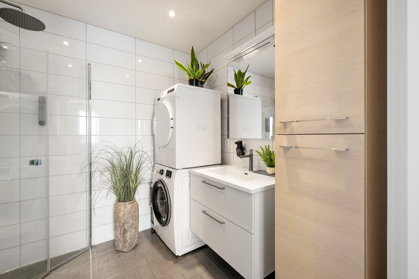 Badet har fliser på gulv og vegger. Innredningen består av et underskap/sideskap, servant, speil og armatur med stikk og en dusjsone. Galleribilde