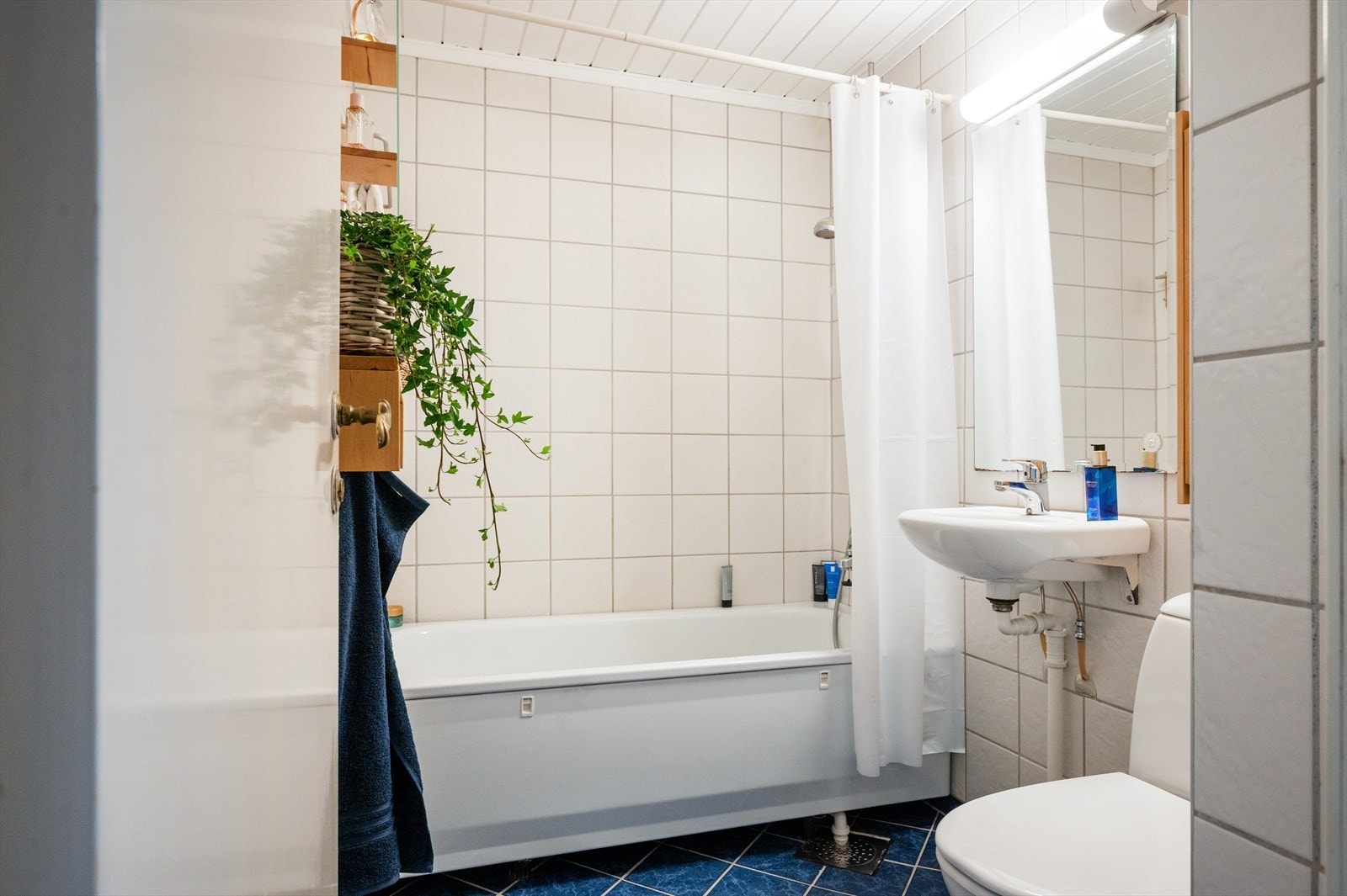 Flislagt baderom med badekar, frittstående toalett og servant. Galleribilde