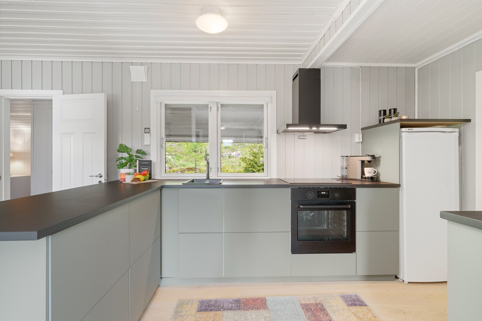 Moderne kjøkkeninnredning med slette fronter, laminatbenkeplate og nedfelt platetopp med stekeovn. Galleribilde