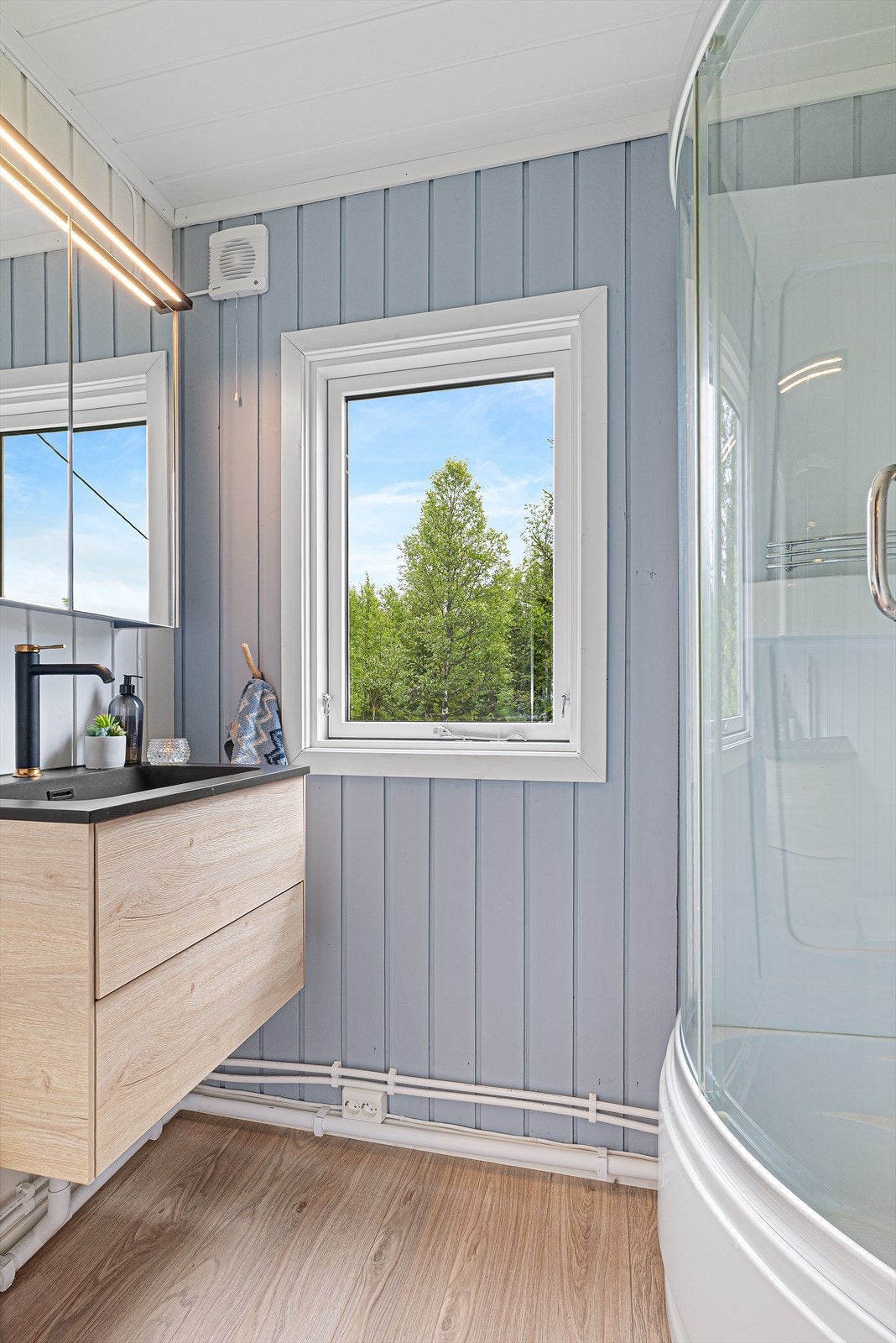 Badet er utstyrt med dusjkabinett, servant med oppbevaring og speil med belysning. Galleribilde