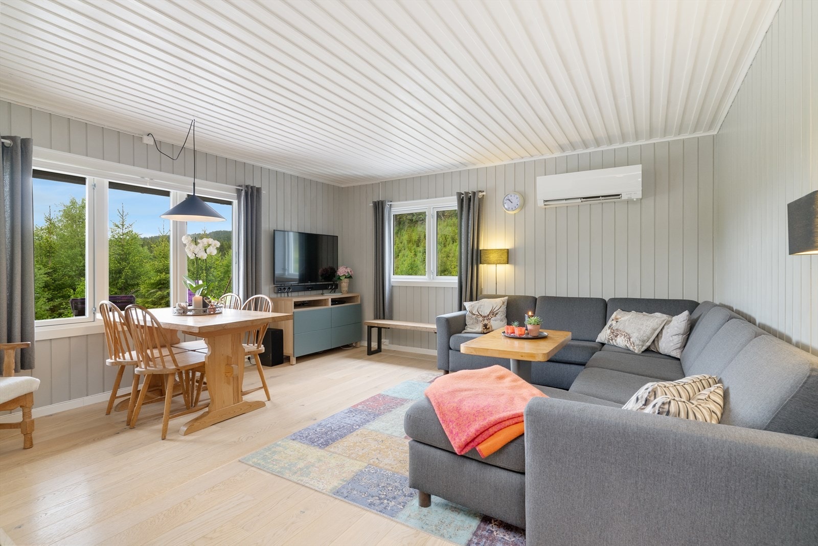 Stuen har plass til både sofagruppe og spisebord, med store vinduer som rammer inn naturen utenfor. Galleribilde
