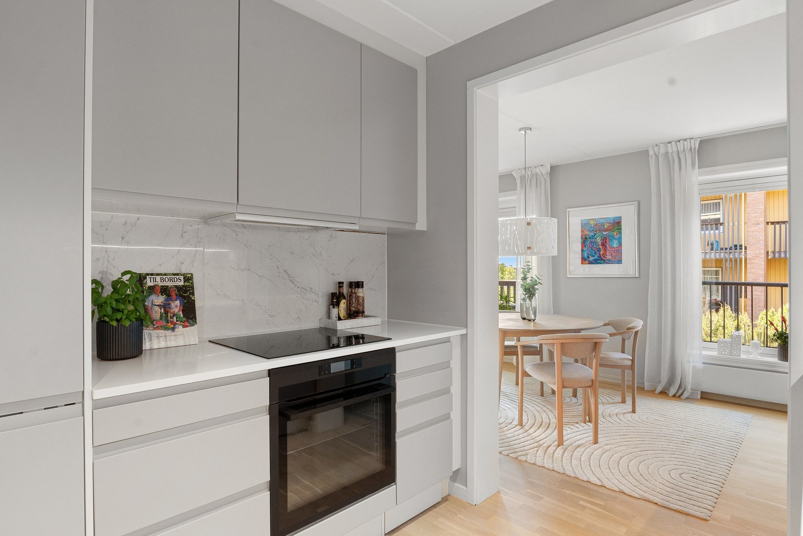 Ny innredning fra NOREMA med glatte, fabrikklakkerte fronter, Corian benkeplate, kum i rustfritt stål, LED-lyslist under overskap og fliser på vegg. Galleribilde