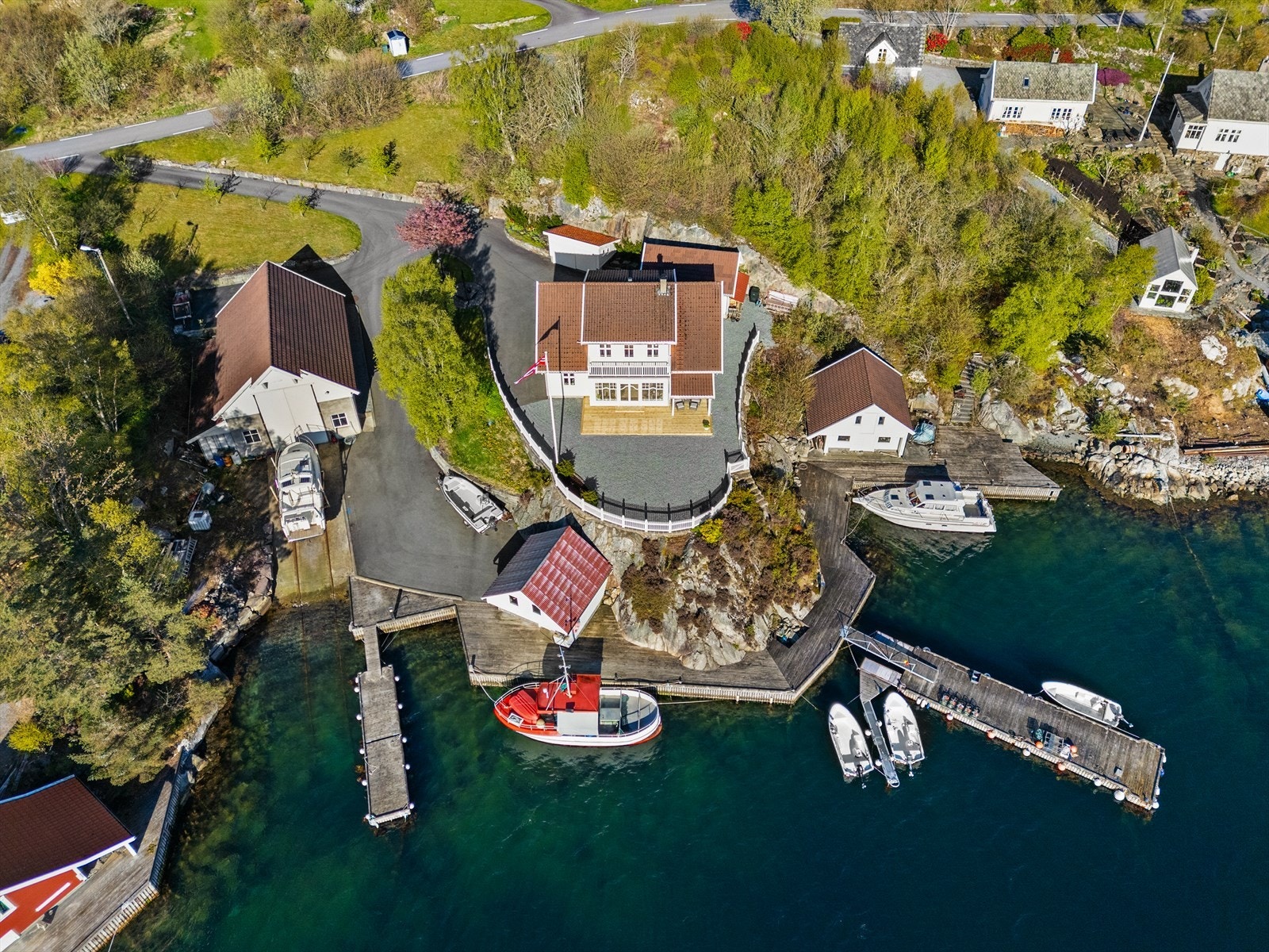 Eiendommen omfatter enebolig, et stort naust/båtverksted regulert for næring, garasje, redskapsbod og egen kai med flytebrygger. Naust med kai og rød båt i front eies av nabo. Galleribilde