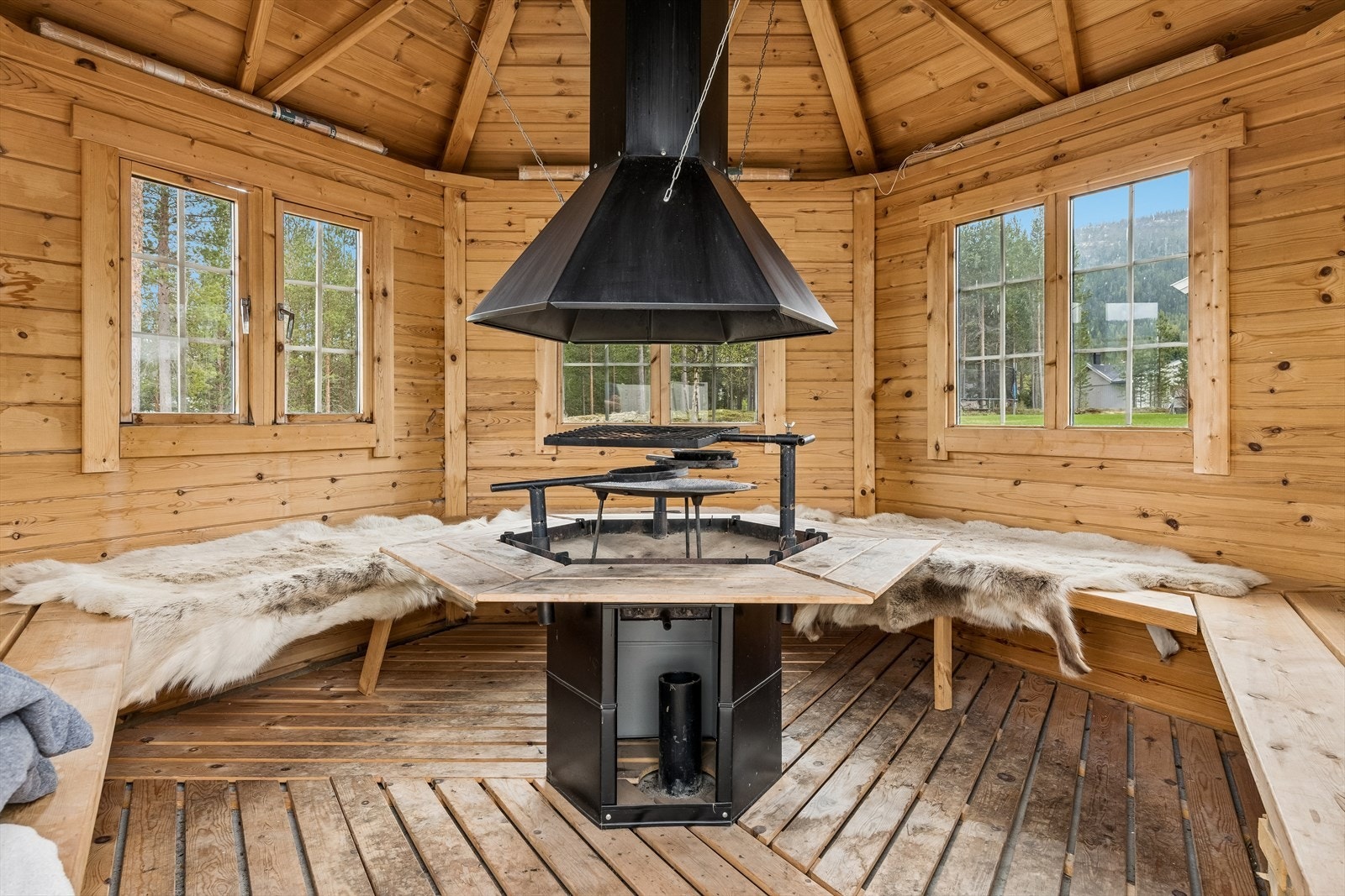 Interiør fra grillhytten, med sittebenker og ildsted i midten. Galleribilde