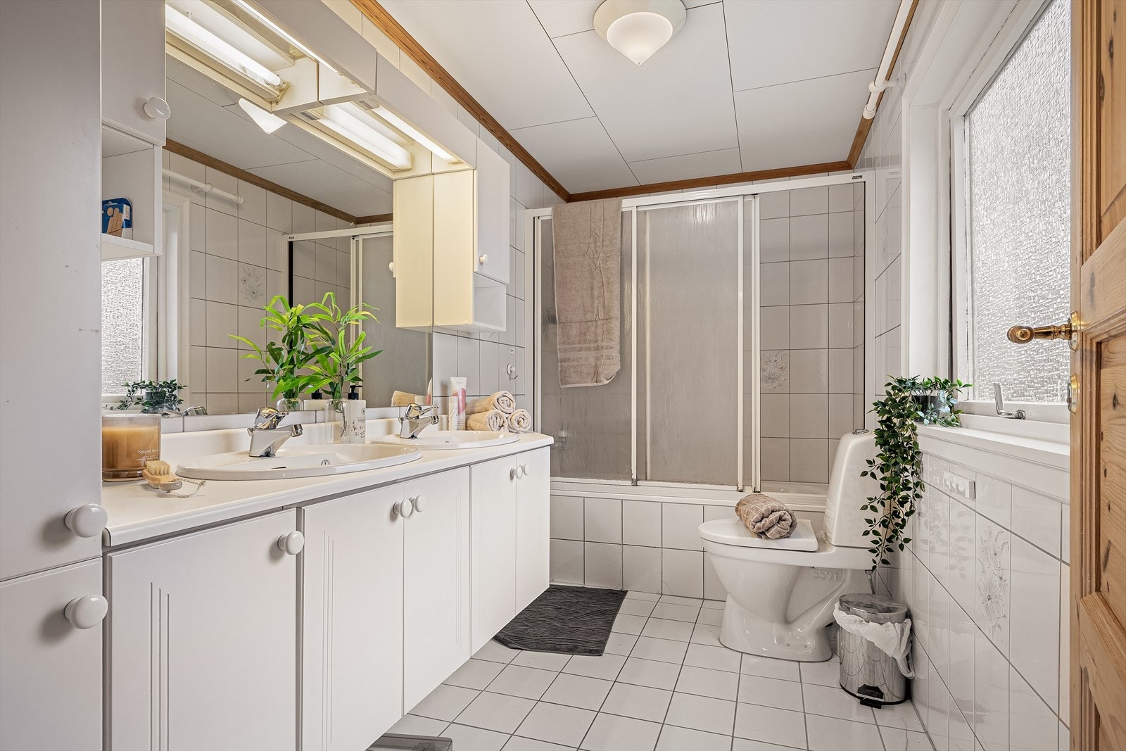 Badet er på ca. 5,0 m² og er innredet med dobbel servant med under- og overskap, veggmontert speil, dusjløsning i innfliset badekar og gulvstående toalett. Galleribilde