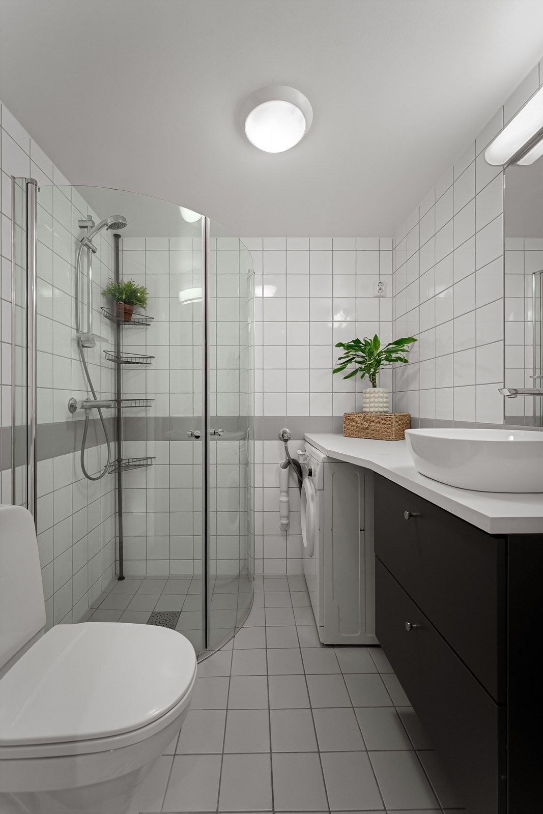 Pent baderom med dusj, wc, speil, servant med skuffer og opplegg for vaskemaskin. Galleribilde