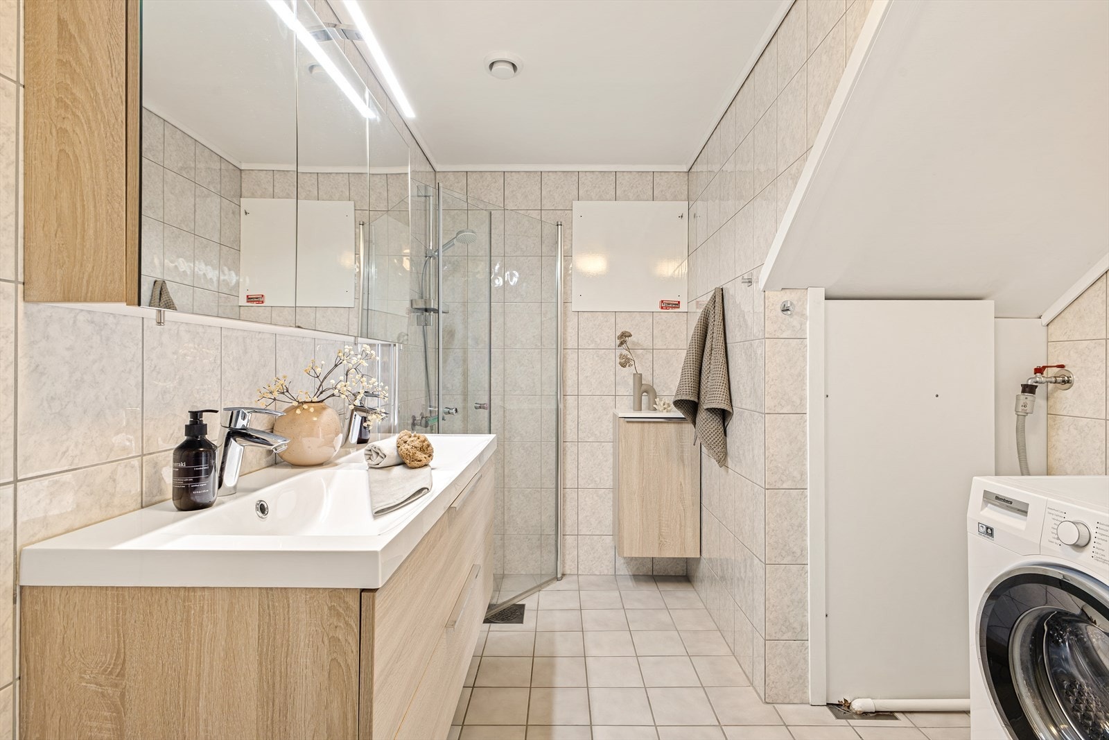 Badet er innredet med innfellbart dusjhjørne av glass, klosett, møblement med servant, samt overskap med speilfront og lys Galleribilde