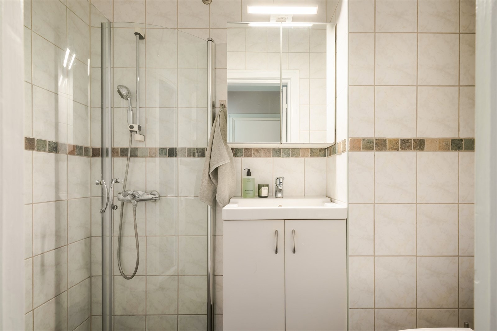 Lyst baderom utstyrt med vegghengt servantinnredning, speil med overlys, dusjvegger i glass og WC. Galleribilde