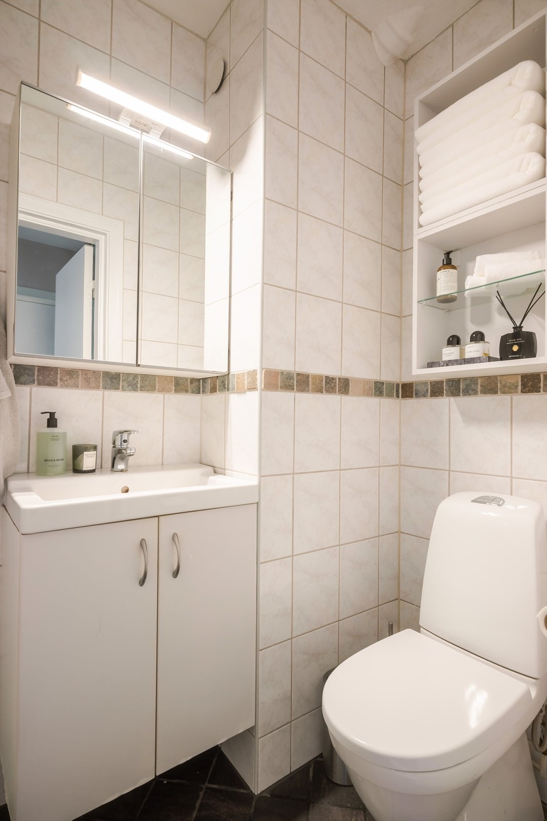 Badet har mørke fliser på gulv, lyse fliser på vegger og malt slett himlig. Galleribilde