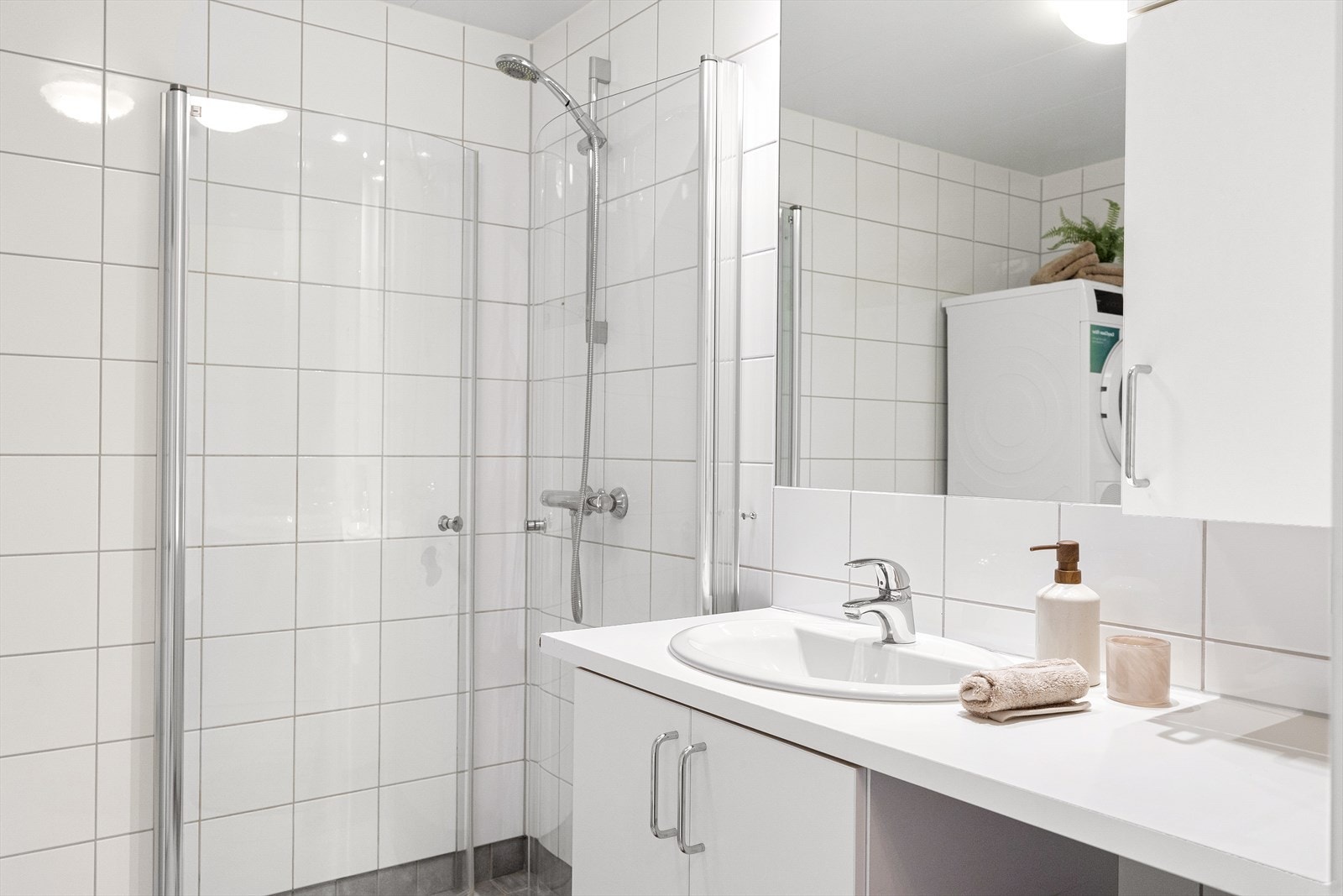 Badet er innredet med servantskap med nedfelt servant og laminat benkeplate, innmurt speil, veggskap, vegghengt toalett samt dusjsone med innfelte dusjdører i herdet glass. Galleribilde