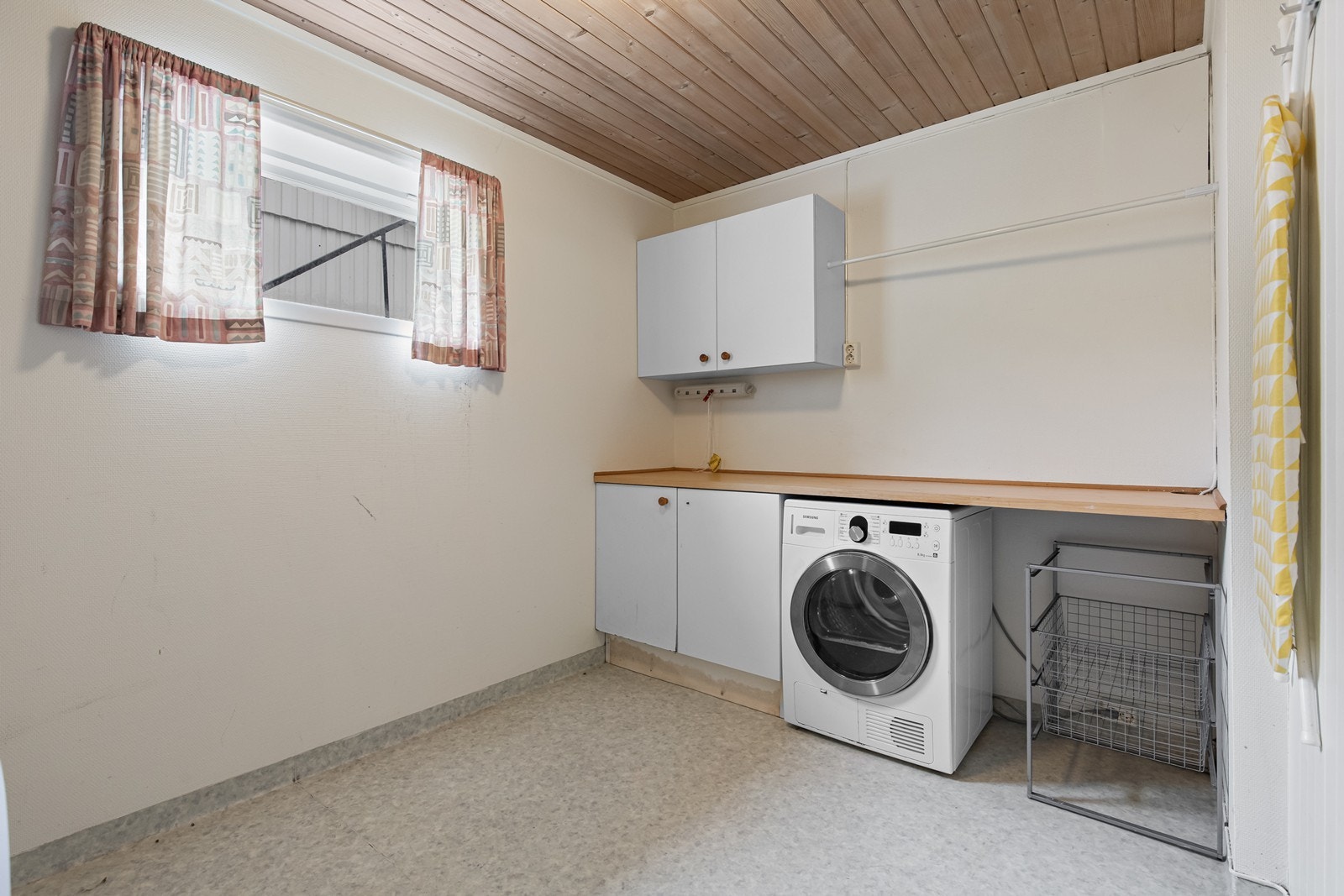 Vaskerommet har belegg på gulv og opplegg for vaskemaskin. Skap for oppbevaring og praktisk benk for bretting av tøy. Galleribilde