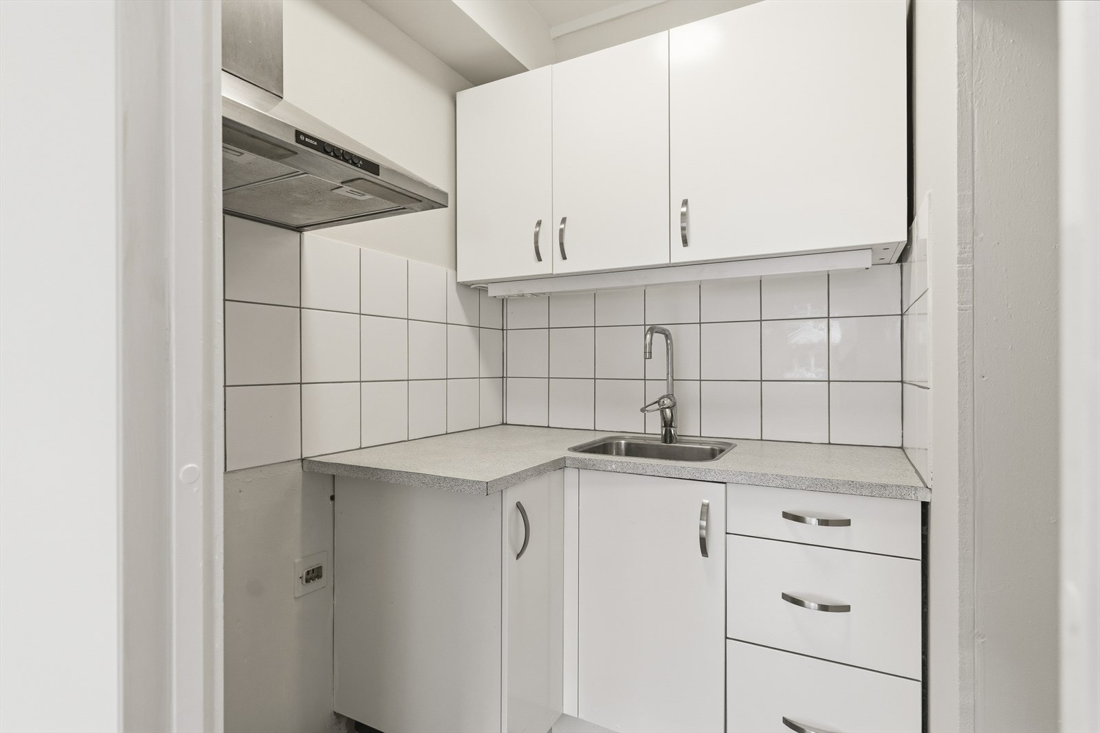 Kjøkkeninnredningen har hvite, slette fronter som gir et tidløst og stilrent uttrykk, kombinert med laminert benkeplate og nedfelt oppvaskkum i stål med tilhørende blandebatteri. Galleribilde