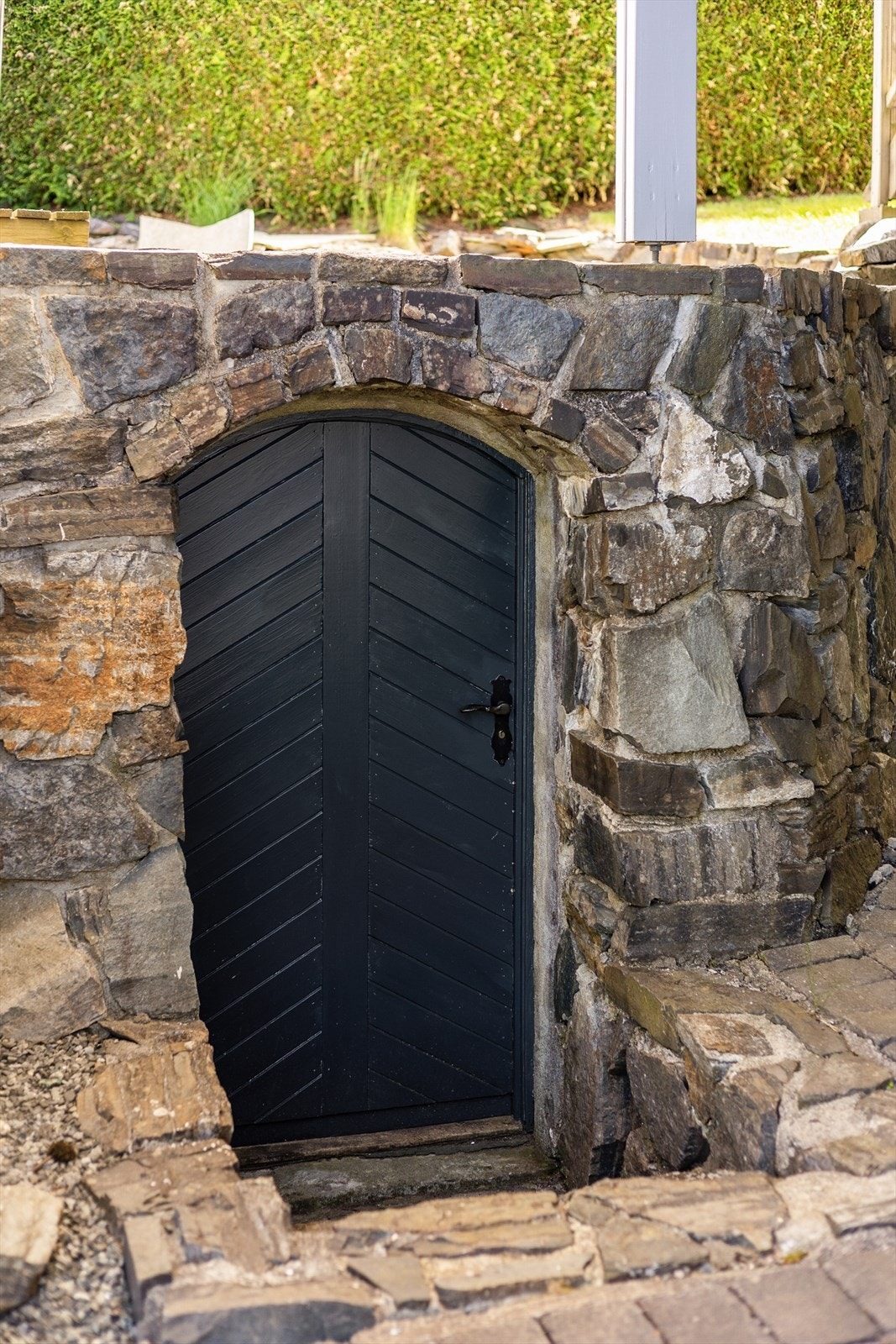 Utvendig bod med adkomst fra gårdsplass, bygget inn i forstøtningsmuren av naturstein - et rom for vinentusiasten? Galleribilde