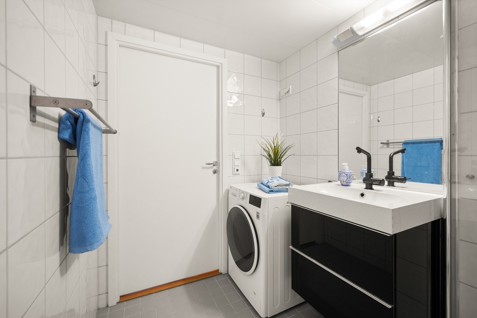 Badet er utstyrt med veggmontert toalett, dusjhjørne med innfellbare glassdører og baderomsinnredning med skuffer, servant med ettgrepsbatteri, speil og belysning. Galleribilde