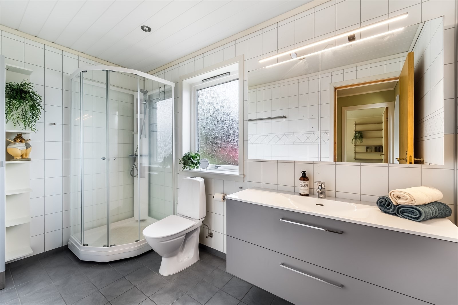 Badet i hovedetasjen har flislagt gulv og baderoms plater på vegg. Innredet med baderomsinnredning, toalett og dusjkabinett. Galleribilde