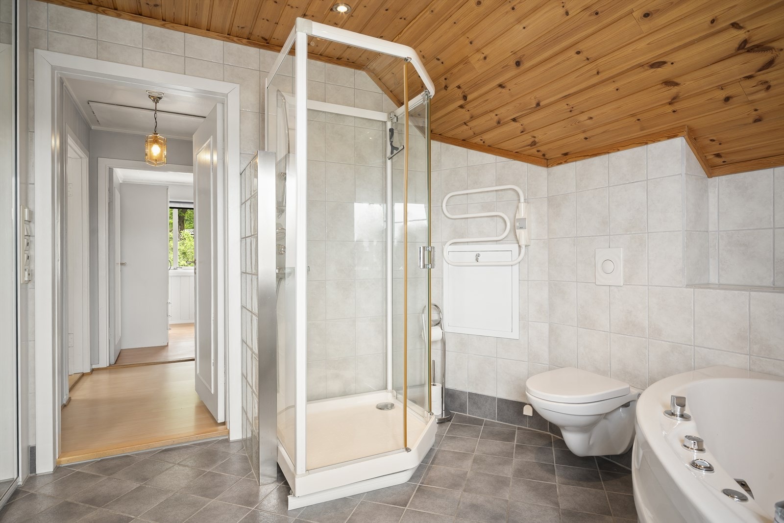 Badet er utstyrt med dusjkabinett, vegghengt toalett, badekar og servant med innredning. Galleribilde