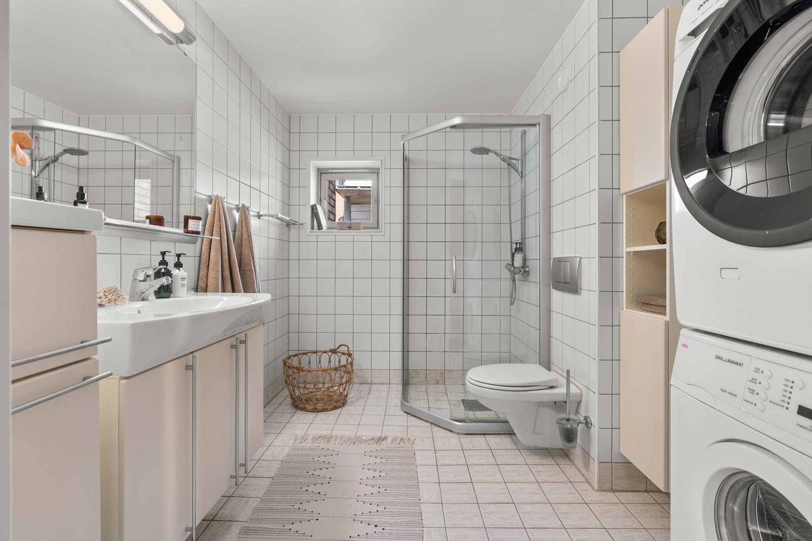 Flislagt bad med behagelig gulvvarme. Badet er innredet med servant i praktisk baderomsinnredning med glatte fronter og tilhørende speil over. Videre er rommet utstyrt med toalett og dusjløsning på gulv. Galleribilde