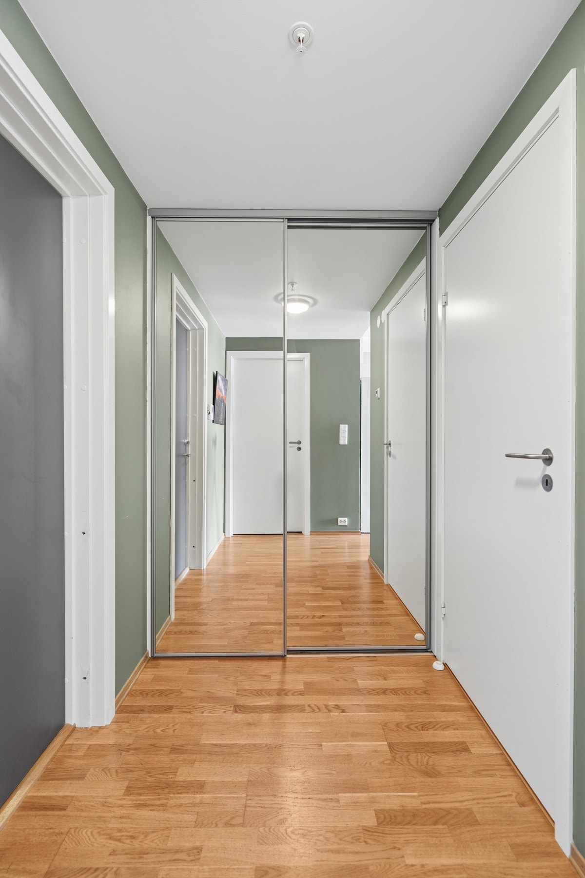 Entré med parkettgulv som er gjennomgående i leiligheten. Skyvedørsgarderobe med speildører gir god plass til oppbevaring. Galleribilde