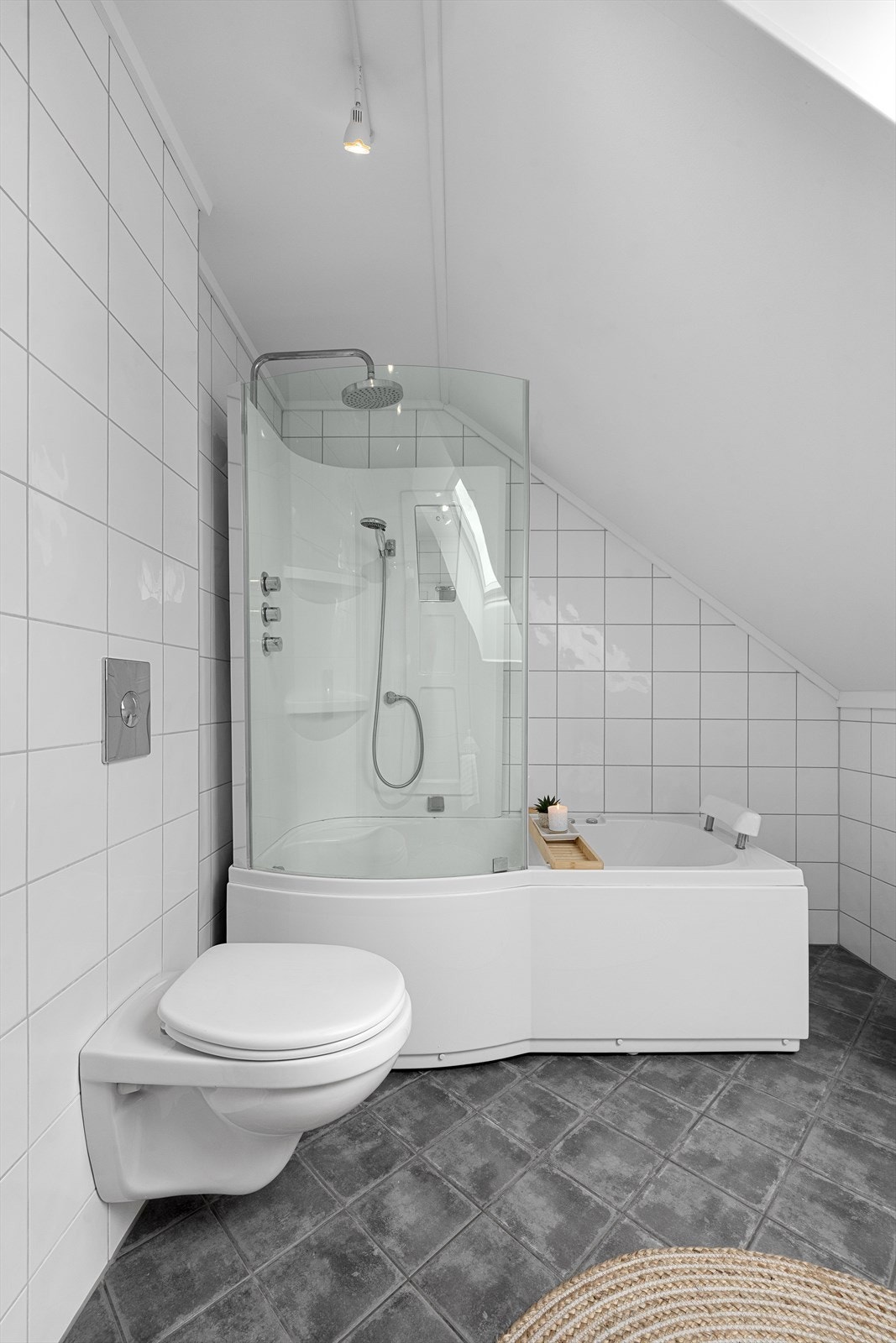 Det er innredet med badekar kombinert med en moderne glassvegg og dusjarmatur med både hånddusj og regnfallsdusj. I tillegg er det et elegant vegghengt toalett og en bred, hvit baderomsinnredning med gode skuffer, servant og speil med integrert belysning. Galleribilde