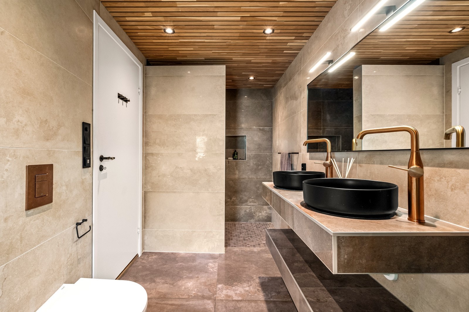 Badet har store, delikate fliser, gulvvarme og spiletak med downlights, samt detaljer i bronsefarget og sort. Galleribilde
