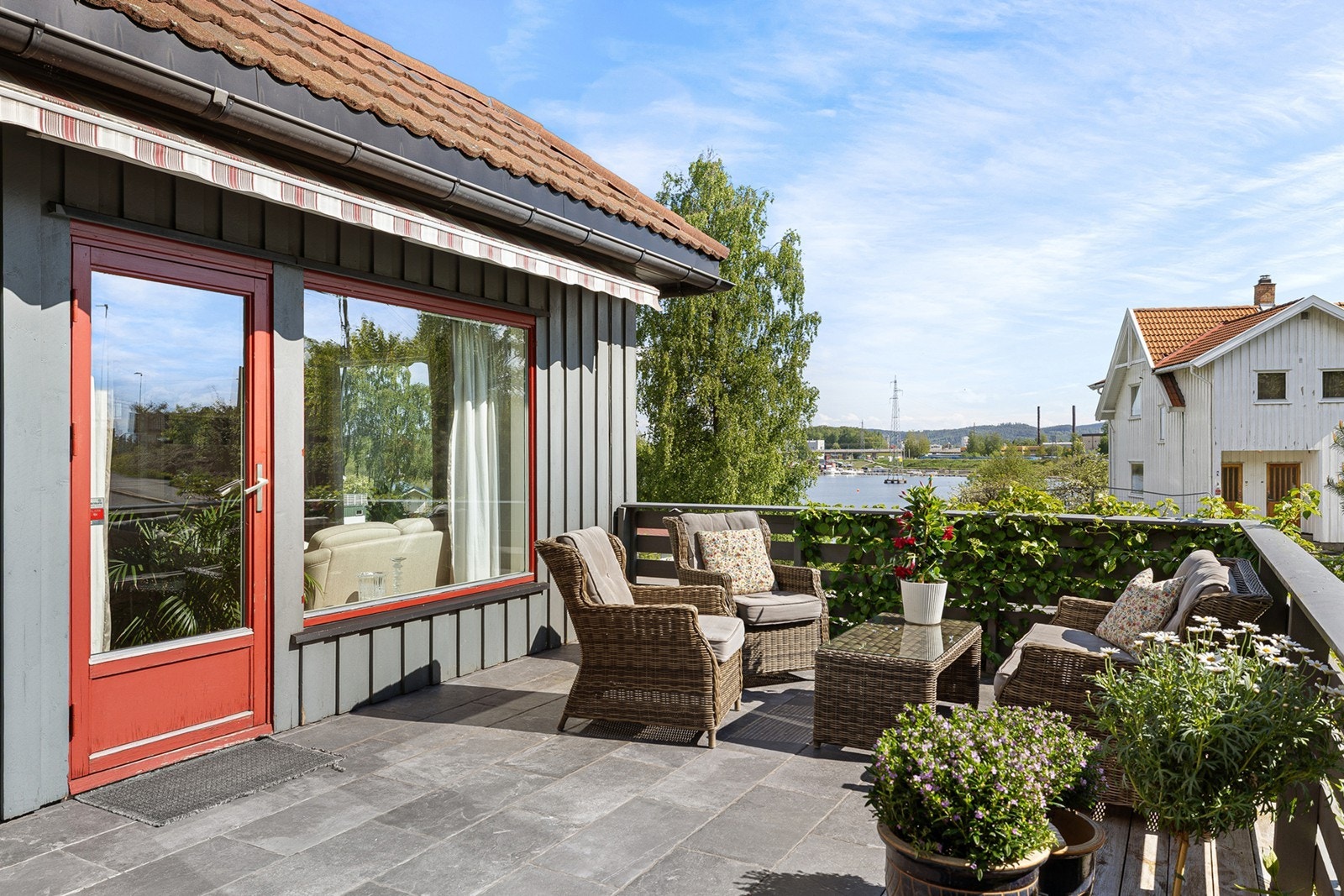 Stor og solrik terrasse med flislagt dekke og markise som gir behagelig skygge på varme sommerdager. Galleribilde