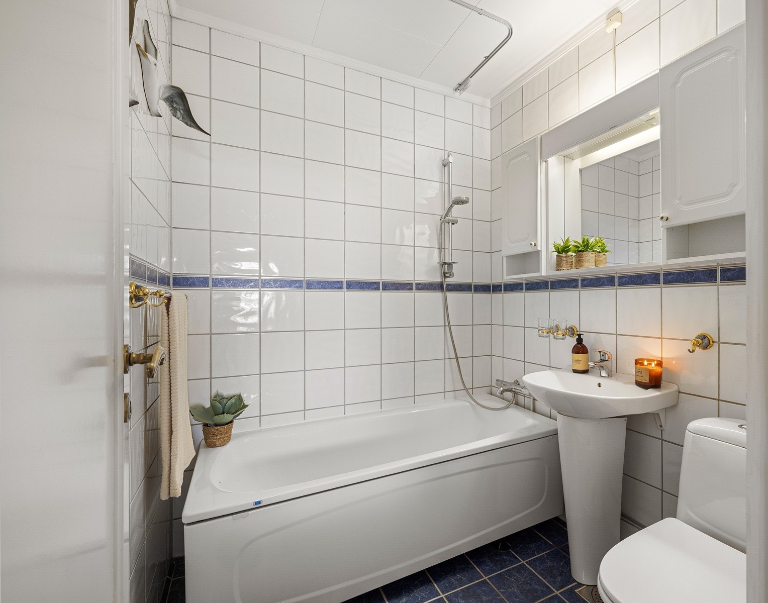 Badet har flislagte gulv og vegger i lyse farger. Rommet er innredet med badekar med dusjløsning. Eldre standard og utførelse, og det må påregnes oppgraderinger for å tilfredsstille dagens krav og forventninger til våtrom. Galleribilde