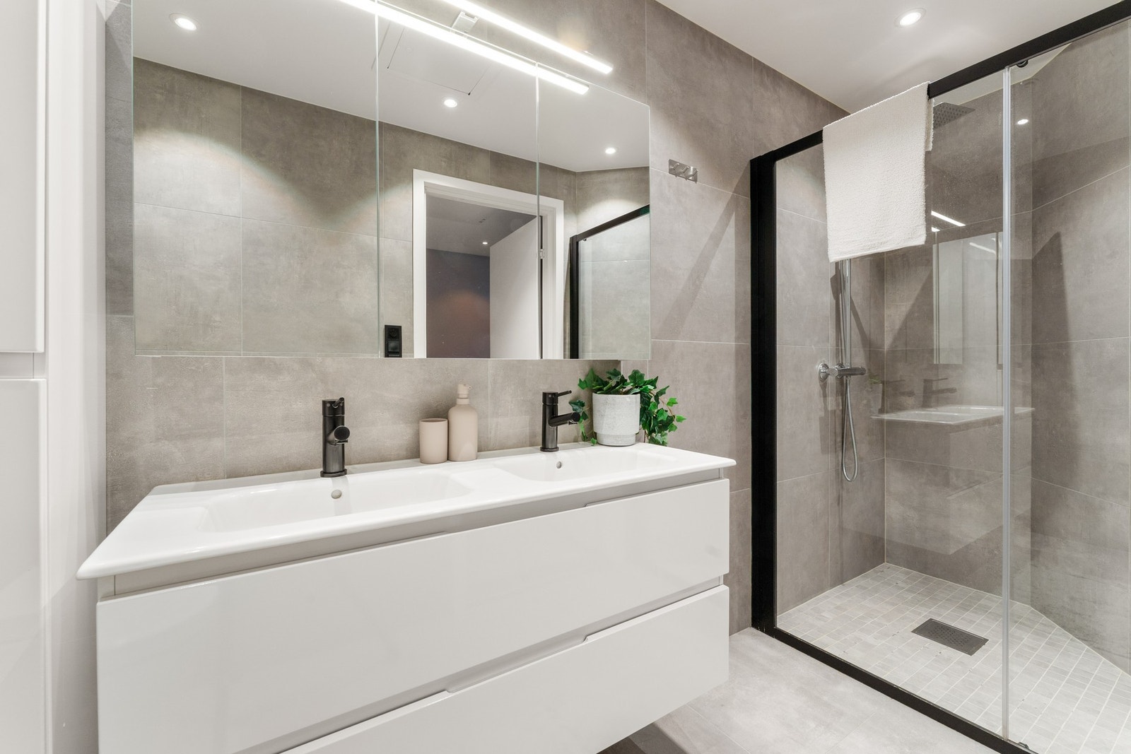 Badet i 1. etasje er utstyrt med heldekkende dobbelservant, dusj med inntreksbare skyvedører, veggehengt toalett og belyst speil. Galleribilde