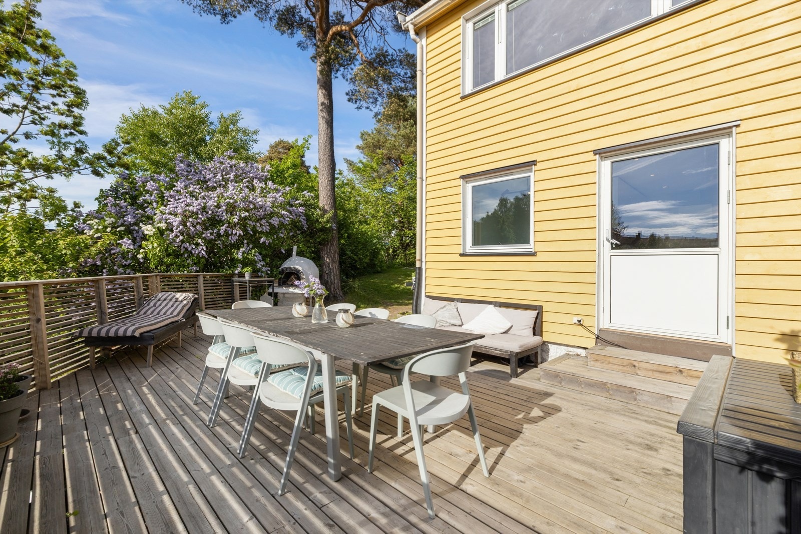 Terrassen har vestvendt beliggenhet. Plass til spisebord, solseng og pizzaovn. Syriner i full blomst og frodig hage rundt. Galleribilde