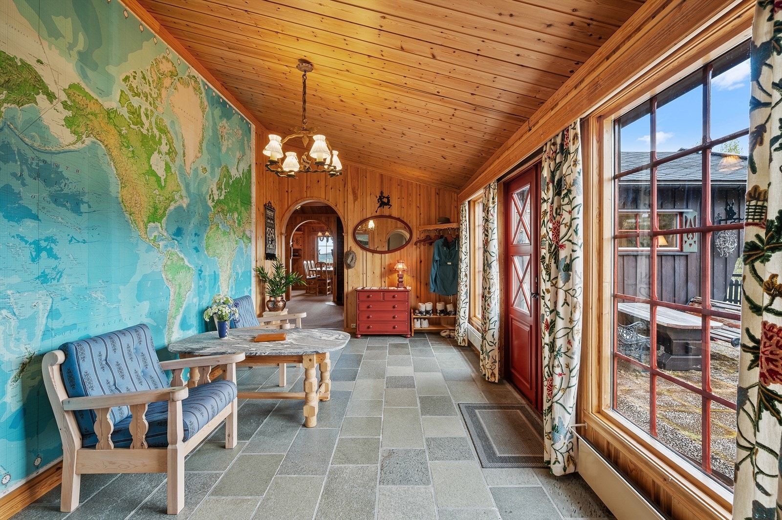 Romslig hall med skifferstein på gulv og store vinduer mot terrassen. Gir et luftig og lyst første inntrykk av hytta. Galleribilde