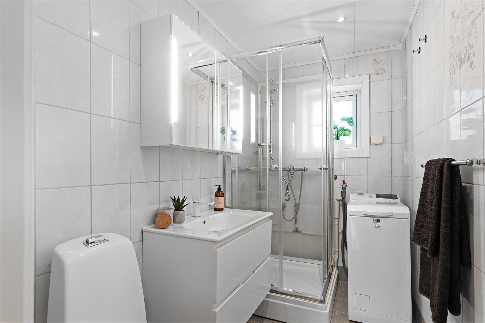 Flislagt bad på 3,8 m² med ferdig opplegg for vaskemaskin, flott baderomsinnredning og dusjkabinett. Galleribilde