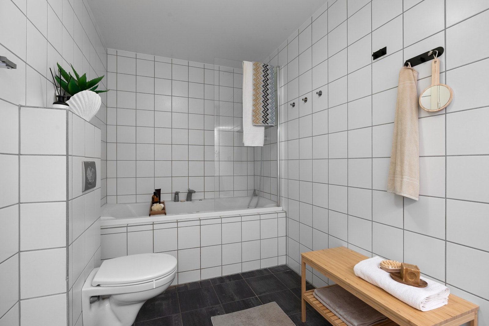 Flislagt bad med badekar og dusjløsning. Et stort bad hvor man har god plass. Vegghengt toalett. Galleribilde
