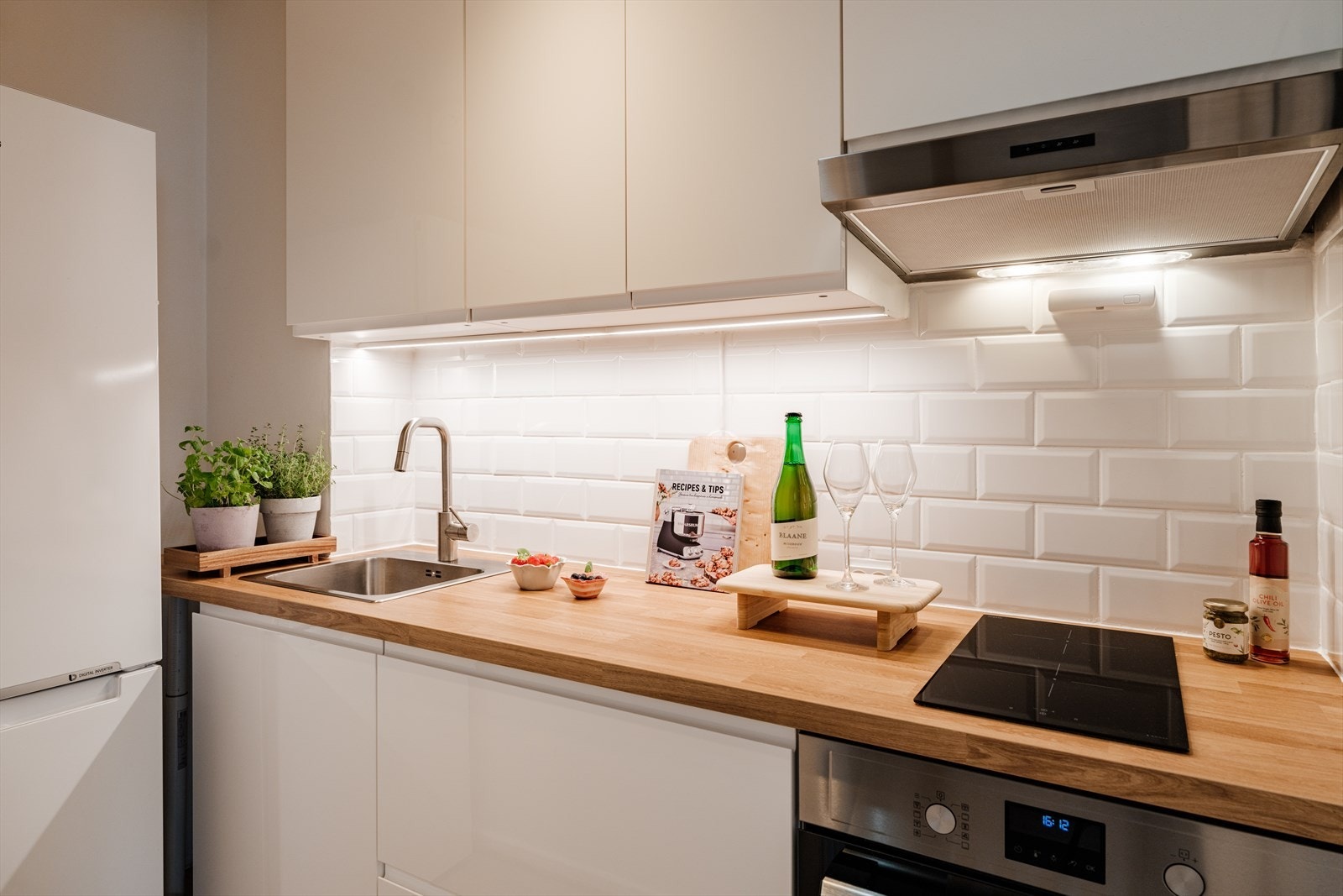 Over benkeplaten er det malte, glatte veggflater som bidrar til et helhetlig og moderne preg. Kjøkkenet er godt utstyrt med platetopp, stekeovn, kombinerte kjøl-/fryseskap. Videre er det opplegg for benkoppvaskmaskin Galleribilde