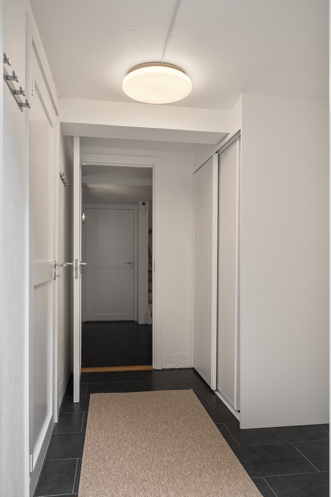 Gang i underetasje med flislagt gulv og skyvedørsgarderobe Galleribilde