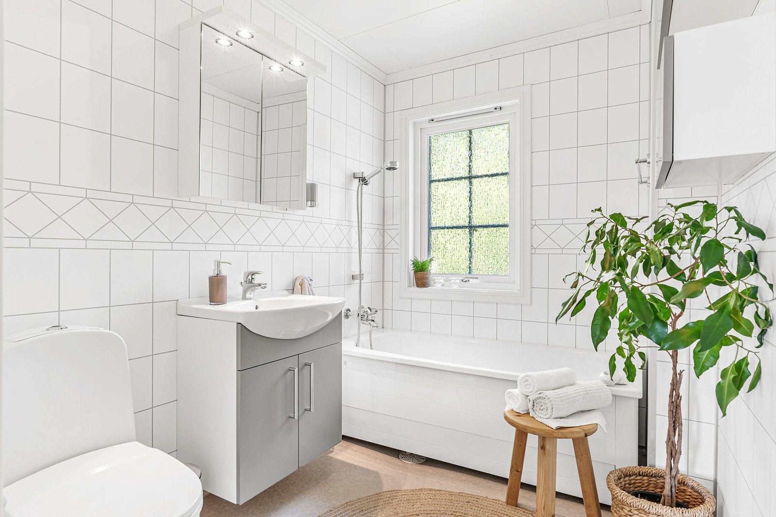 Badet har gulvbelegg med varmekabler og baderomsplater på vegg, samt badekar og baderomsinnredning med vask. Galleribilde