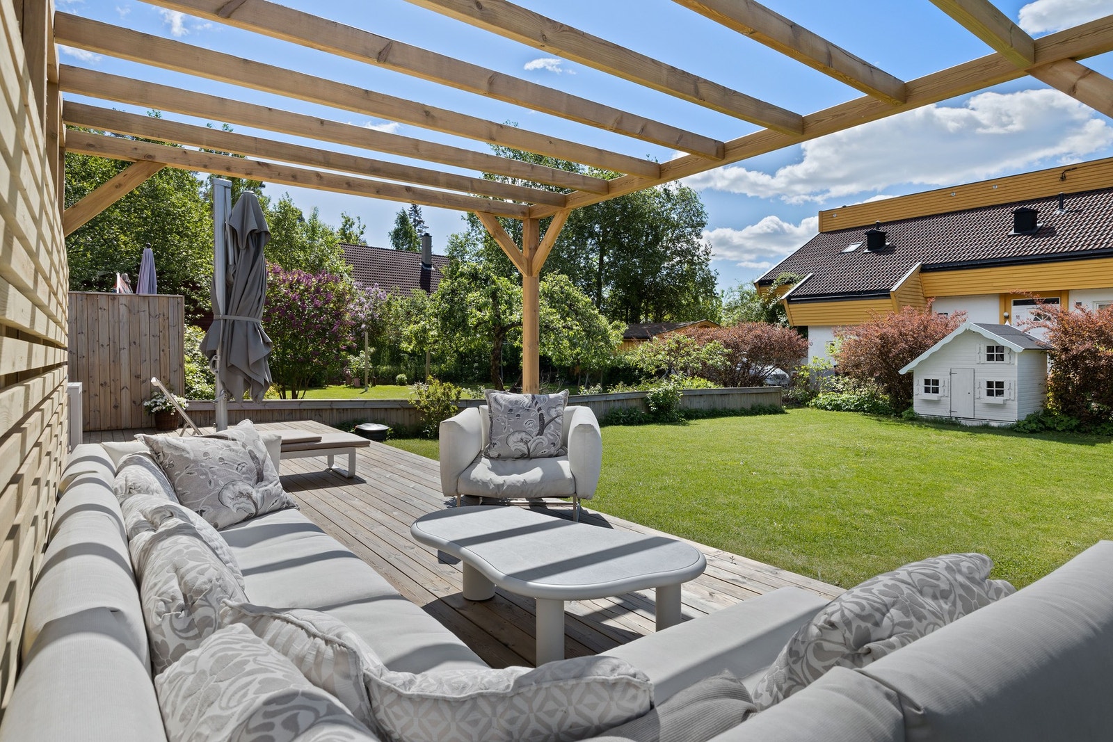 Skjermet uteplass med pergola og utsyn mot den grønne hagen. Galleribilde