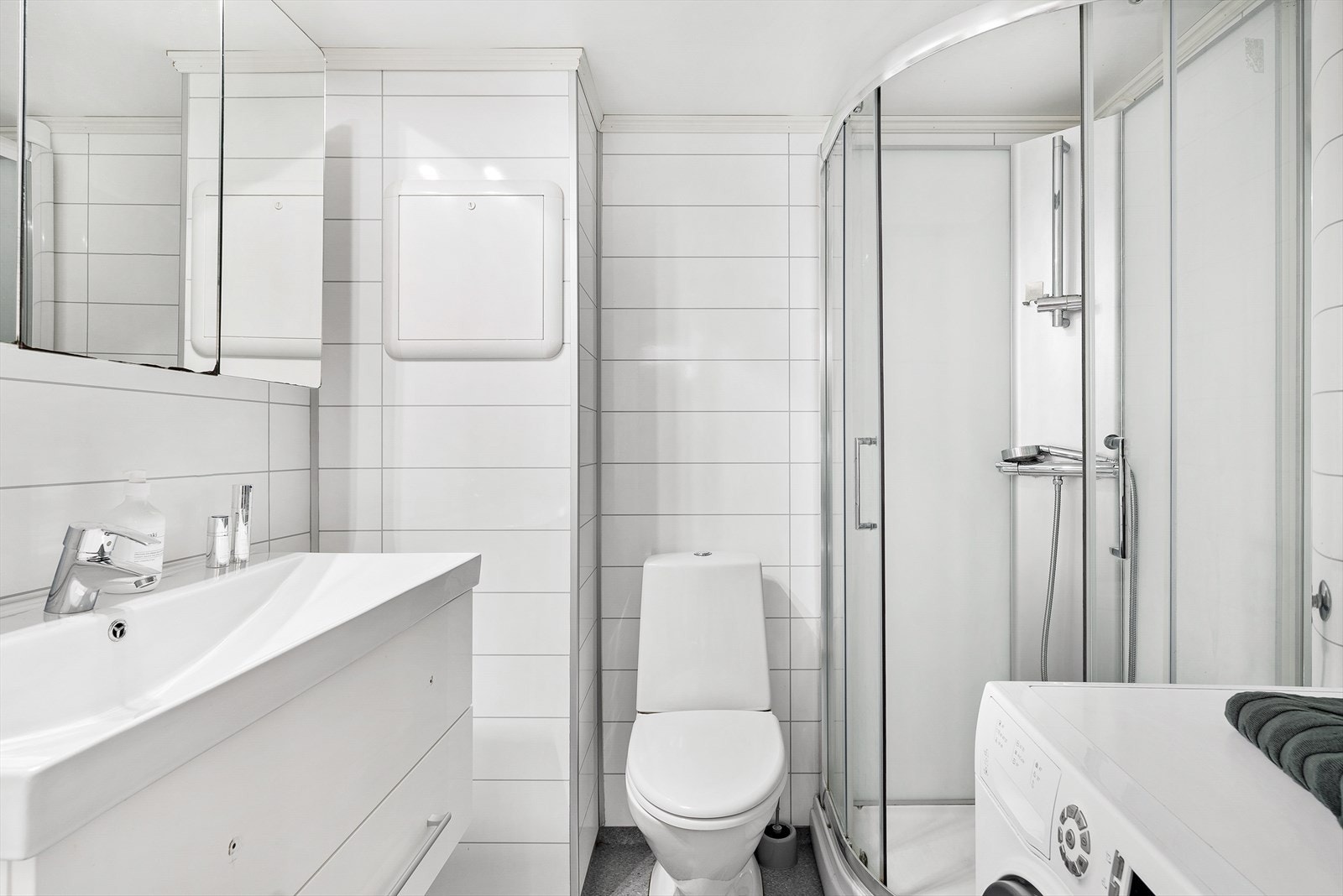 Pent bad med vinylbelegg på gulv og baderomsplater i flisimitasjon på vegger (badet er godkjent iht. byggetegninger) - Rommet har toalett, dusjkabinett, opplegg for vaskemaskin og baderomsinnredning Galleribilde