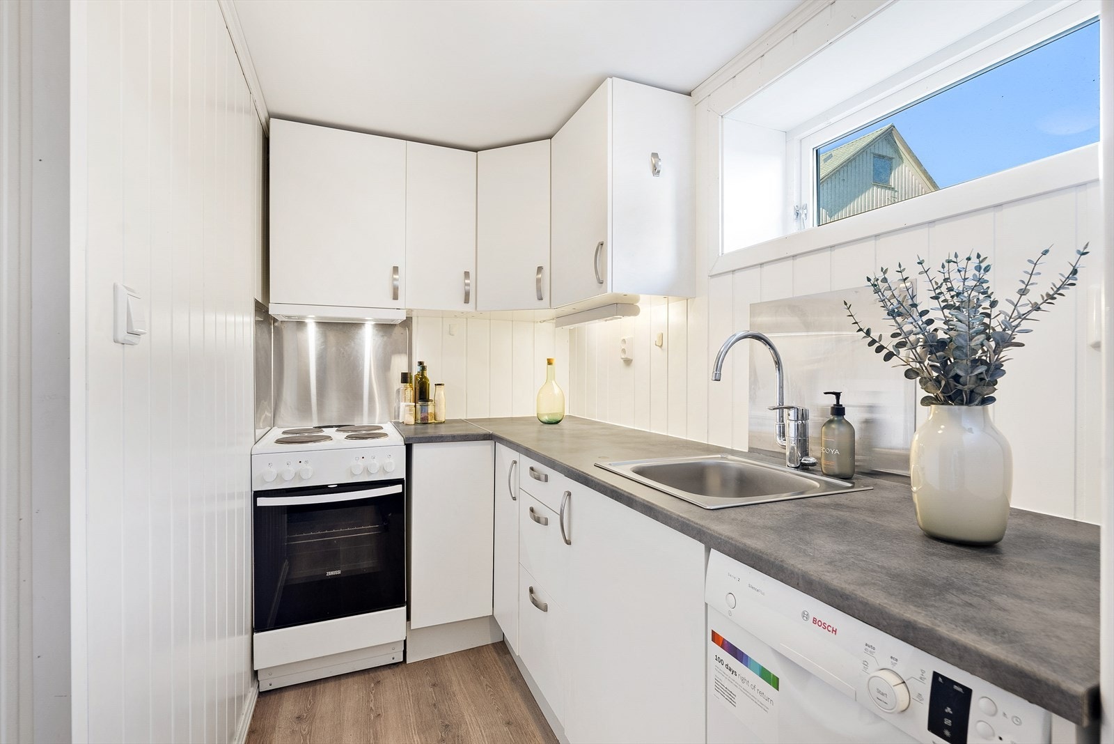 Kjøkkenet har innredning med hvite slette fronter og benkeplate i laminat - Hvitevarene medfølger og består av komfyr, oppvaskmaskin og kombiskap kjøl/frys Galleribilde