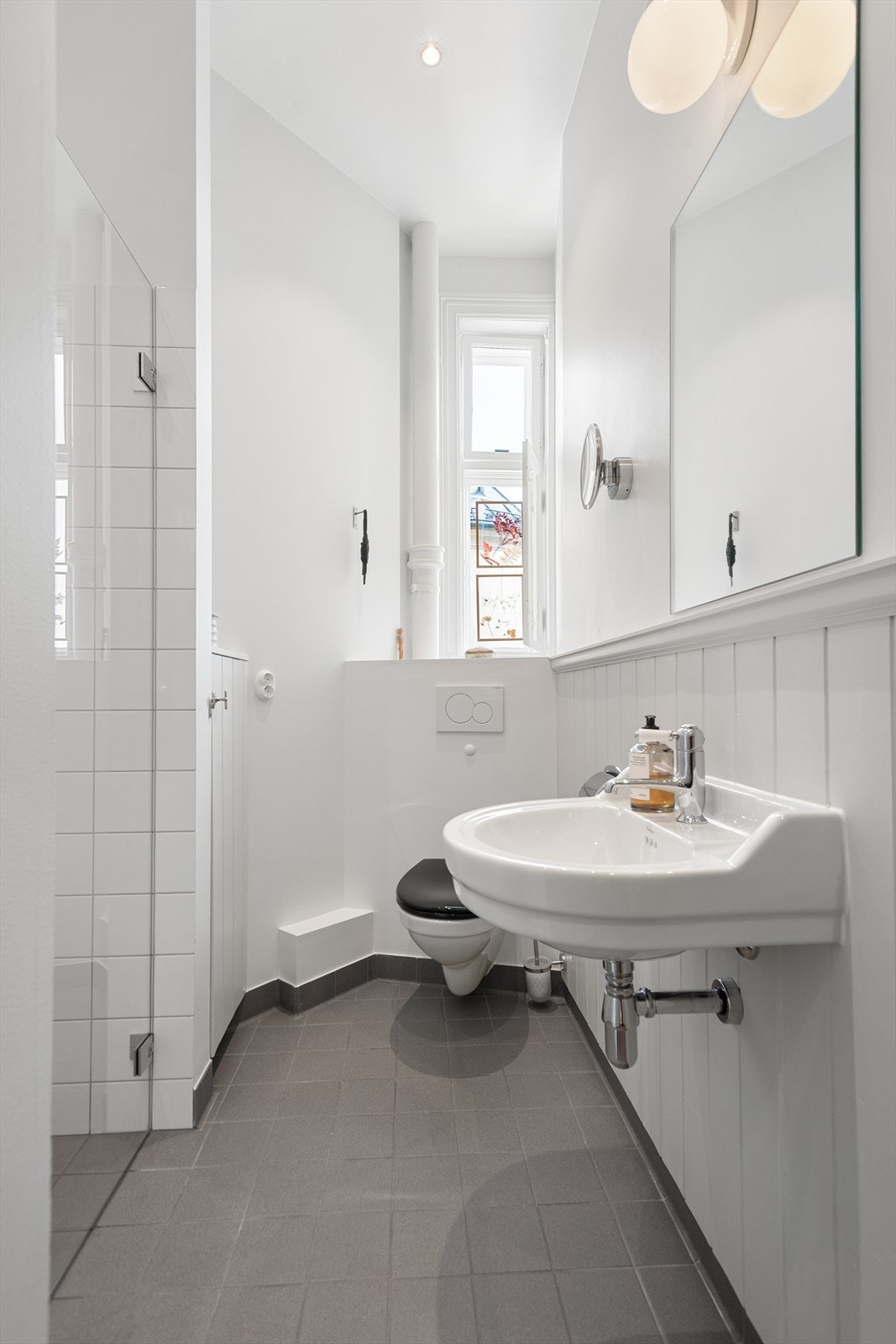 Leiligheten har et nyoppusset baderom fra 2024 med flislagt gulv med varmekabler og downlights i himling - Badet har et klassisk, tidløst uttrykk med vegger bestående av delvis fliser og delvis malt trepanel med flislagt oppkant Galleribilde