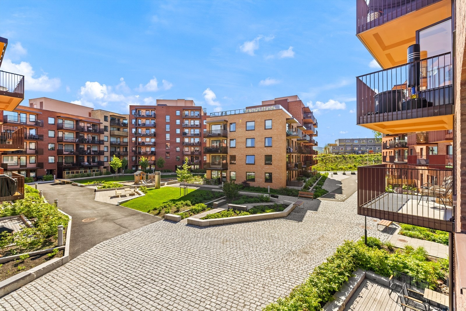 Leiligheten vender mot et rolig og moderne gårdsrom med grønne fellesarealer og hyggelige oppholdssoner. Gårdsrommet er lyssatt på kveldstid. Galleribilde