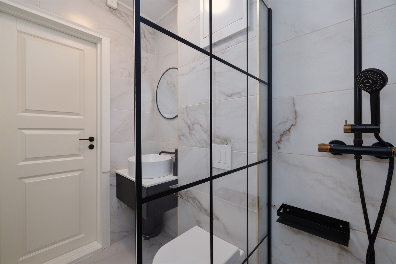 Badet har flislagte overflater, vegghengt toalett og dusjhjørne med glassfelt. Galleribilde