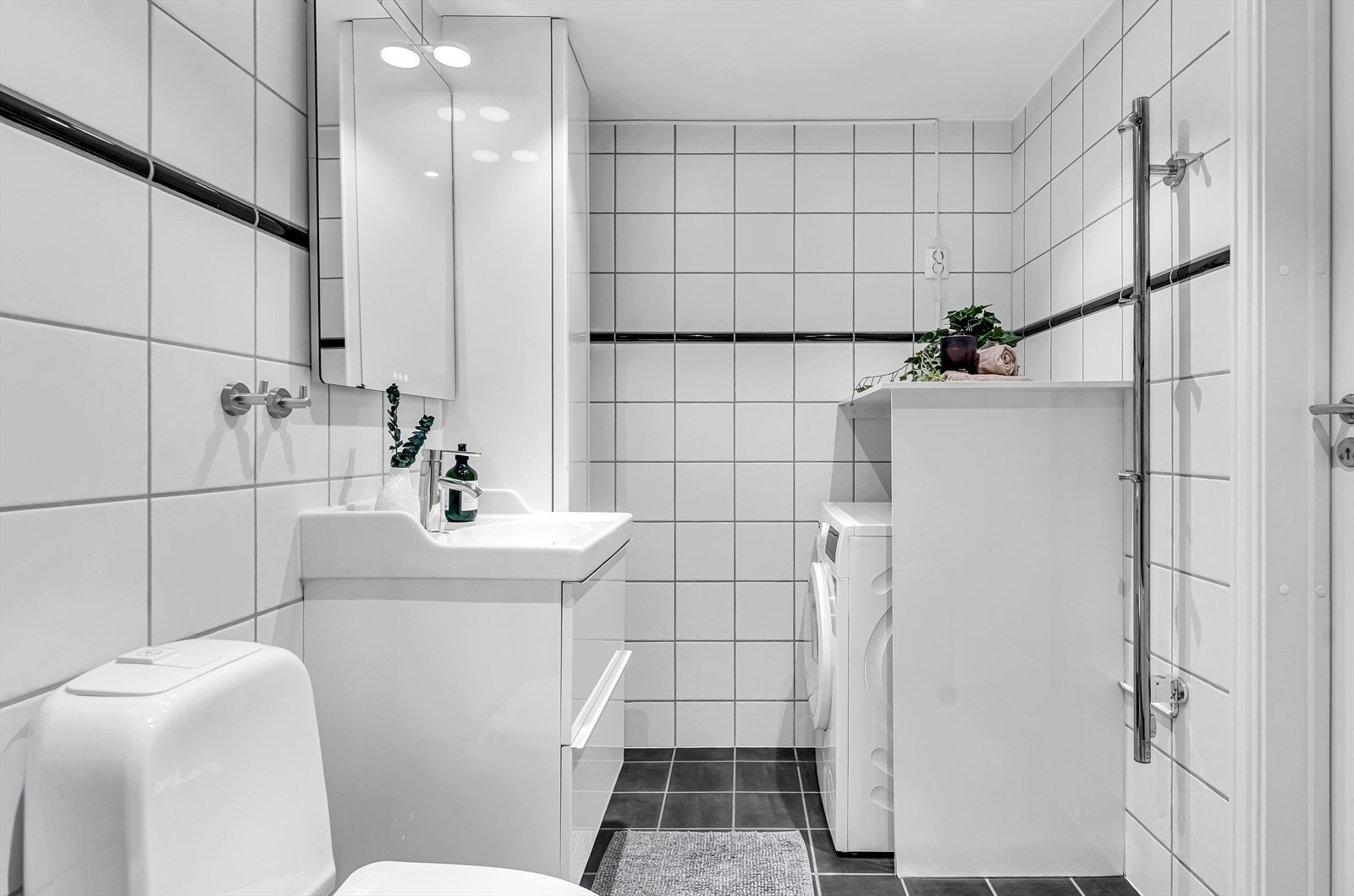 Badet er utstyrt med badekar med dusjvegg i glass, servantskap med servant og ettgreps blandebatteri, gulvmontert toalett samt opplegg for vaskemaskin. Galleribilde