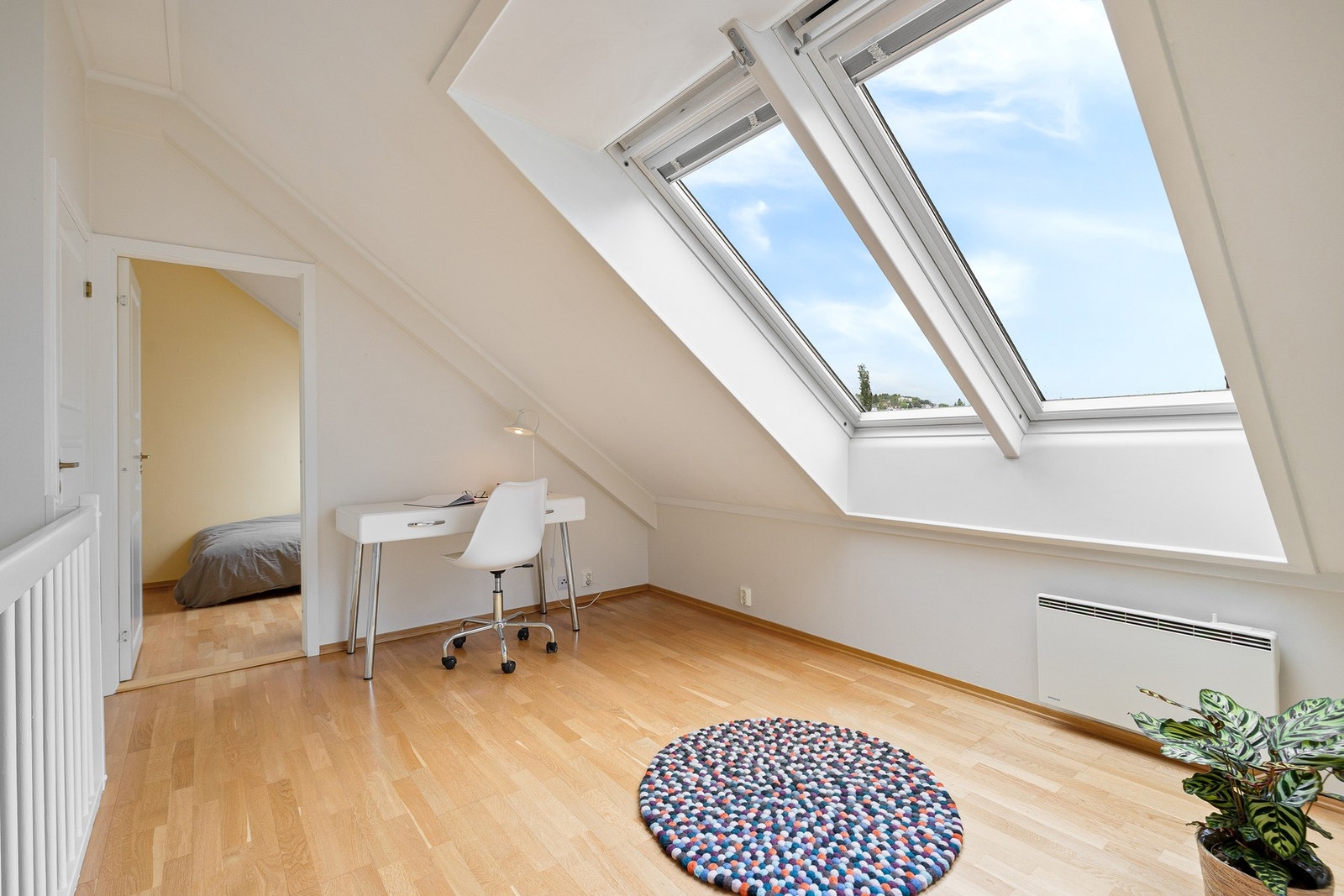 Loftsstuen preges av karakteristiske takvindu som slipper inn rikelig med naturlig dagslys og skaper en innbydende og luftig atmosfære. Legg merke til plassbygde plisségardiner i vinduene. Galleribilde