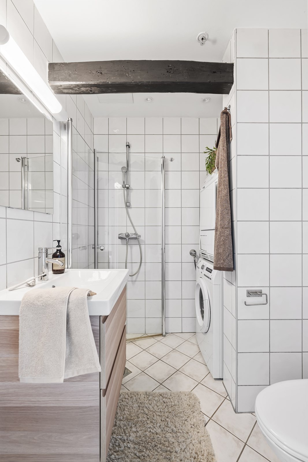 Fislagt baderom med opplegg til vaskemaskin. Badet består av dusjnisje, veggheng servant med underskap, vegghengt speil og gulvstående WC Galleribilde