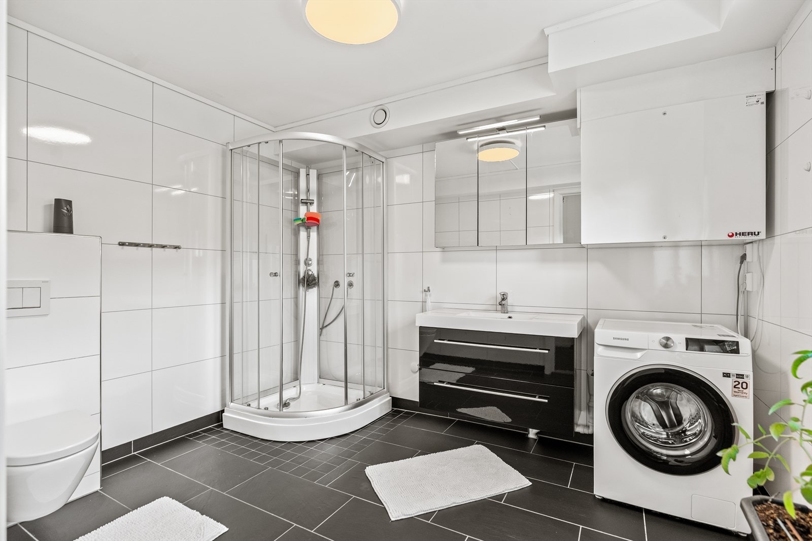 Badet er pent innredet med flislagte gulv og vegger, dusjkabinett, servant, vegghengt toalett, skap med speil og opplegg for vaskemaskin. Galleribilde
