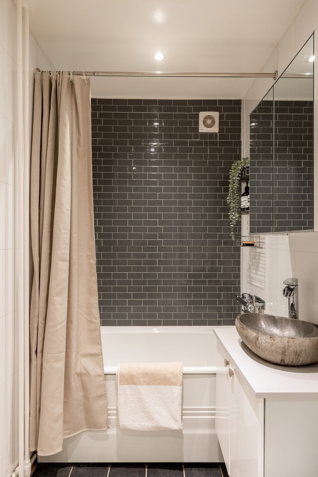 Badet er innredet med klosett, servant plassert på innredning, speilskap og badekar med dusj og forheng. Galleribilde