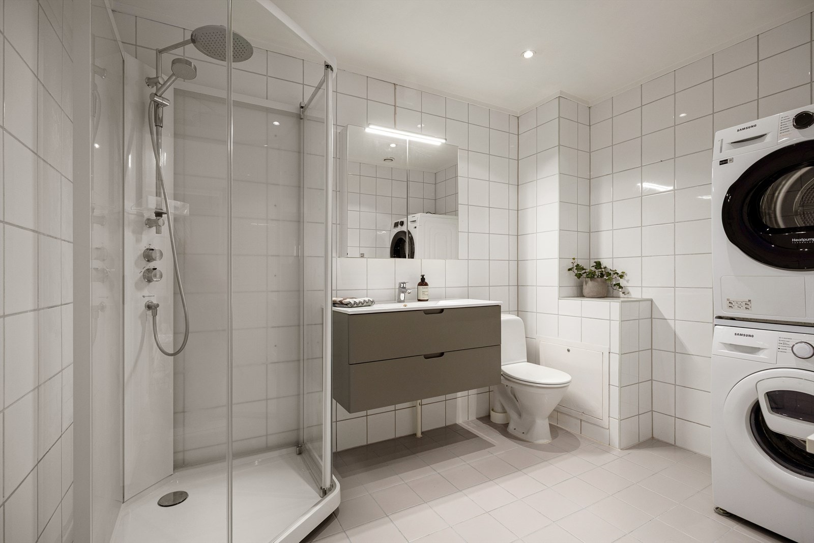 Stort og flislagt bad med dusjkabinett, servant med skuffer, speilskap og wc. Vaskemaskin og tørketrommel på badet medfølger. Galleribilde