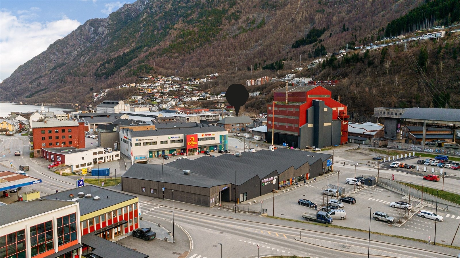 Eiendommen har en sentral beliggenhet ved Rema 1000 (bygg i forgrunnen), Coop Extra (hvitt bygg) og kollektivknutepunktet/turistinformasjon (rødt bygg like ved) Galleribilde