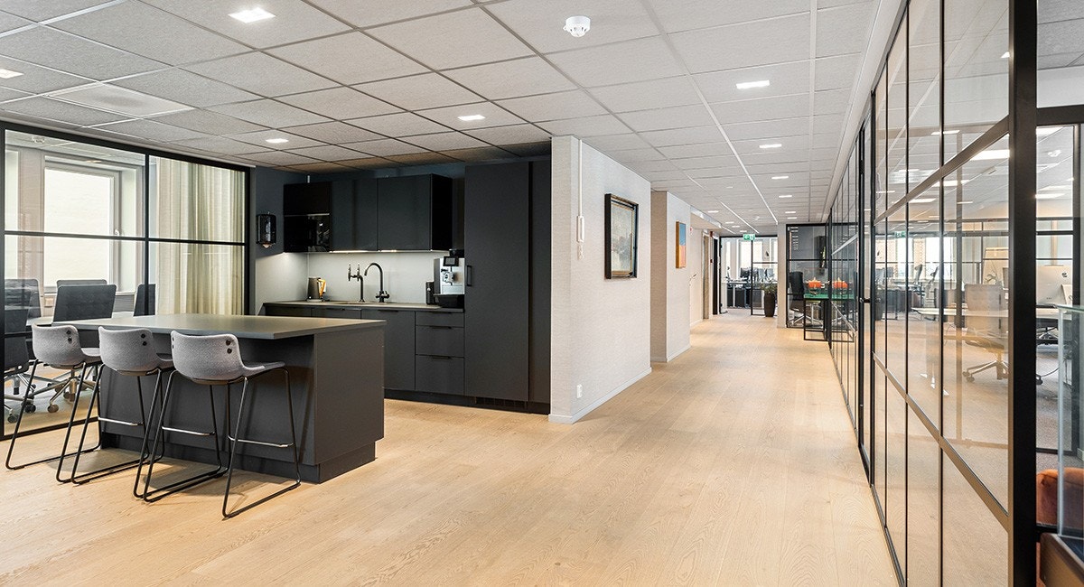 Velkommen inn! Ved inngangsonen er det etablert et møterom og kjøkken til venstre. Teamkontor og cellekontor er plassert på høyre side og kontorlandskapet er rett fram på bildet Galleribilde